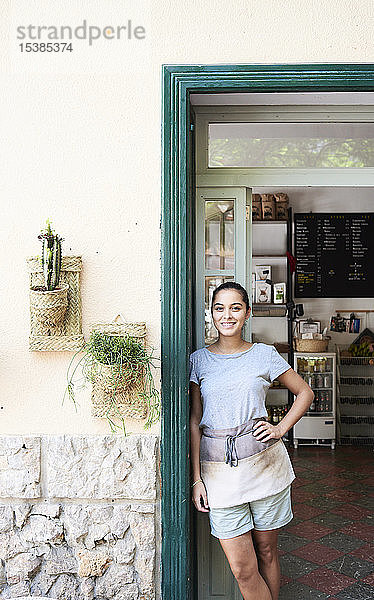 Porträt einer lächelnden Frau  die an der Eingangstür eines Cafés steht