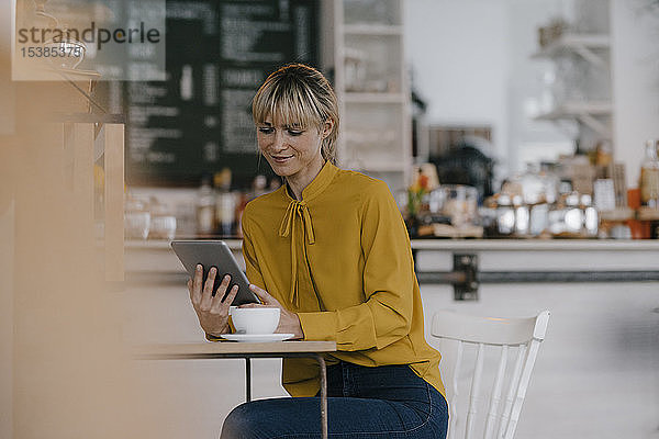 Blonde Geschäftsfrau benutzt Smartphone in einem Café und liest Textnachrichten