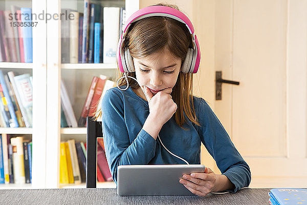 Kleines Mädchen macht Hausaufgaben mit Kopfhörer und digitalem Tablet