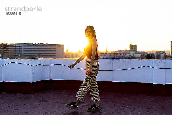 Teenager-Mädchen geht bei Sonnenuntergang auf einer Dachterrasse in der Stadt