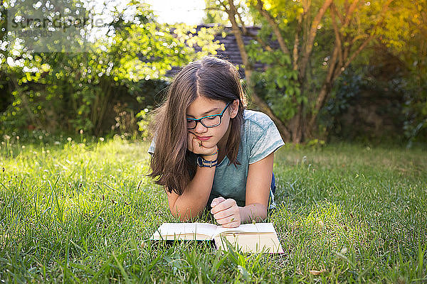 Mädchen liegt auf einer Wiese im Garten und liest Buch
