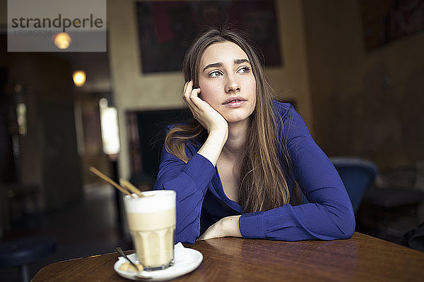 Junge Frau  die in einem Café am Tisch sitzt und zur Seite schaut