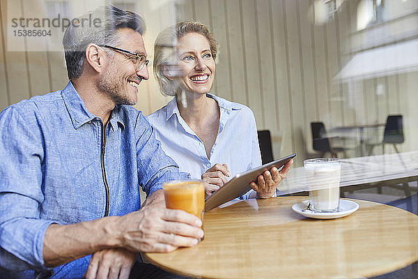 Glückliche Frau und Mann benutzen Tabletten in einem Café