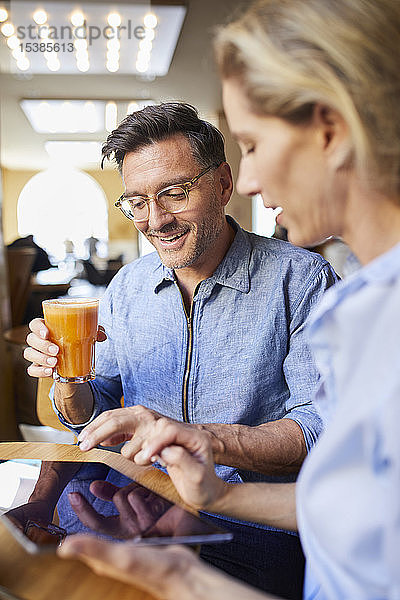 Lächelnde Frau und Mann benutzen Tabletten in einem Café