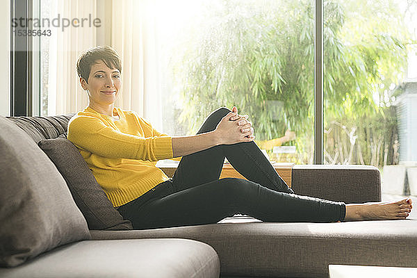 Porträt einer lächelnden Frau  die sich zu Hause auf der Couch entspannt