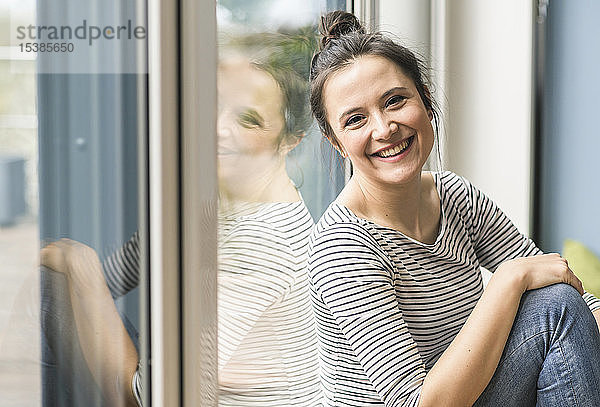 Porträt einer glücklichen Frau  die zu Hause am Fenster sitzt