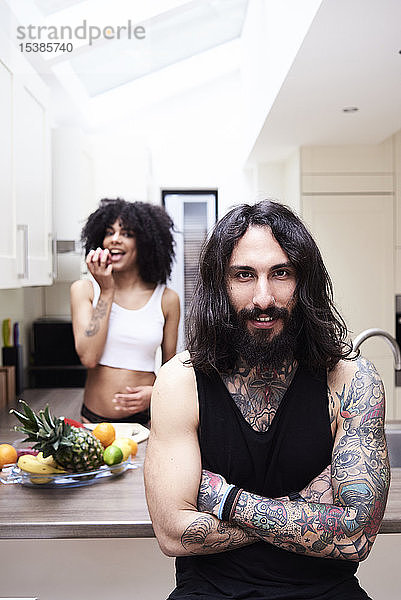 Porträt eines lächelnden tätowierten Mannes mit Freundin in der Küche