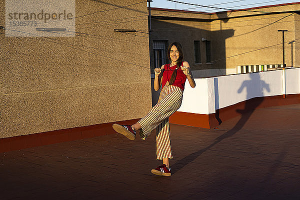 Glückliches Teenager-Mädchen tanzt bei Sonnenuntergang auf der Dachterrasse