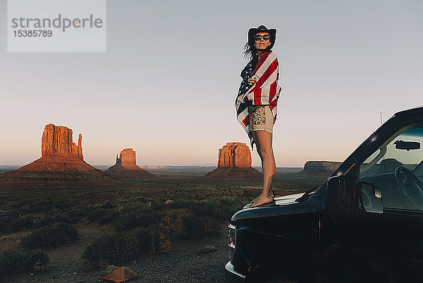 USA  Utah  Monument Valley  Frau mit der Flagge der Vereinigten Staaten von Amerika genießt den Sonnenuntergang im Monument Valley