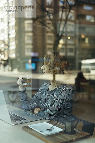 Reife Geschäftsfrau mit einem Laptop mit einem Glas Tee in einem Cafe