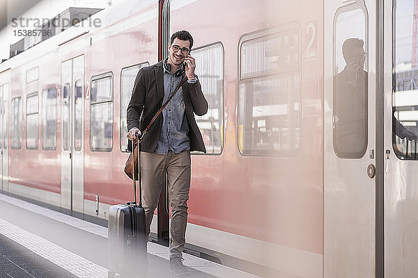 Lächelnder junger Mann mit Handy auf Bahnsteig entlang des S-Bahnsteigs