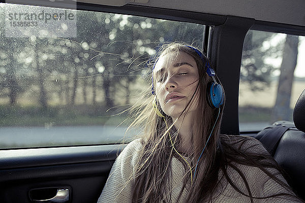Junge Frau mit windgepeitschtem Haar in einem Auto mit Kopfhörern