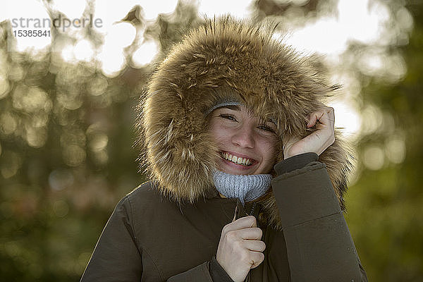 Porträt einer lachenden jungen Frau mit Kapuze mit Pelzbesatz im Winter