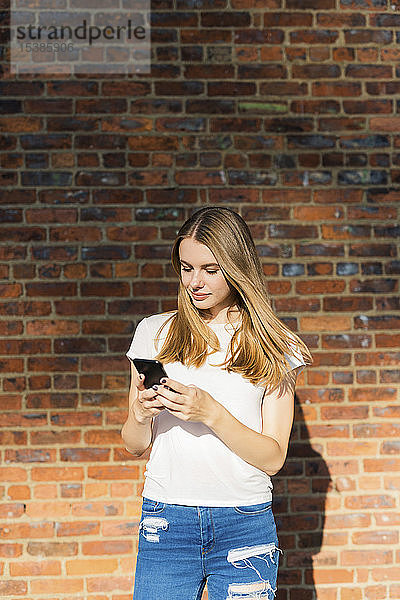 Junge Frau vor Backsteinmauer  mit Smartphone