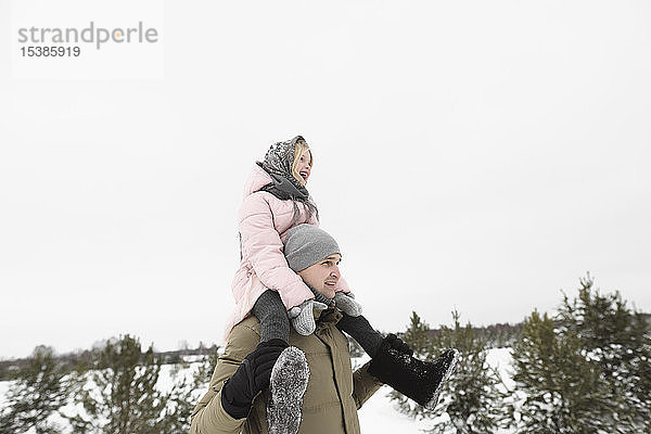 Vater trägt im Winter seine kleine Tochter auf den Schultern