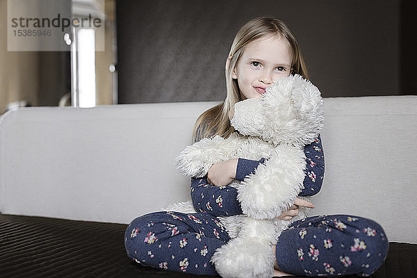 Bildnis eines lächelnden kleinen Mädchens in Pyjama mit Blumenmuster  das einen weißen Teddybär hält