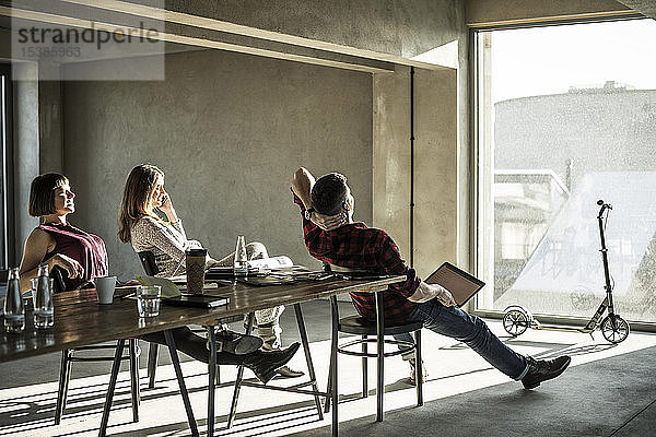Gruppe von Kreativen  die in ihrem Büro sitzen  aus dem Fenster schauen und die Sonne genießen