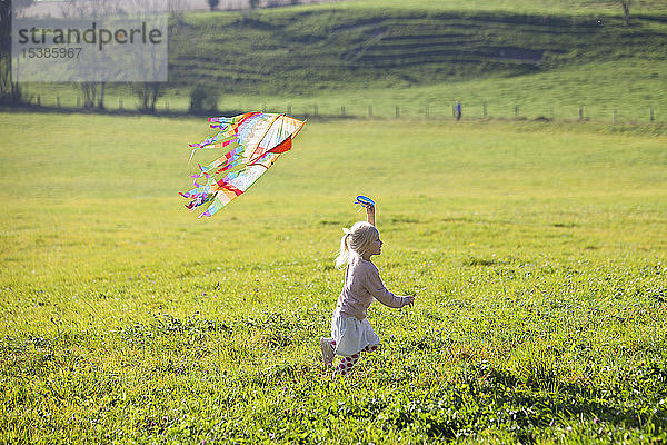 Kleines Mädchen rennt im Feld mit Drachen