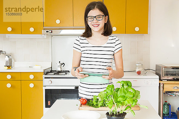 Porträt eines in der Küche stehenden lächelnden Mädchens mit Tablette