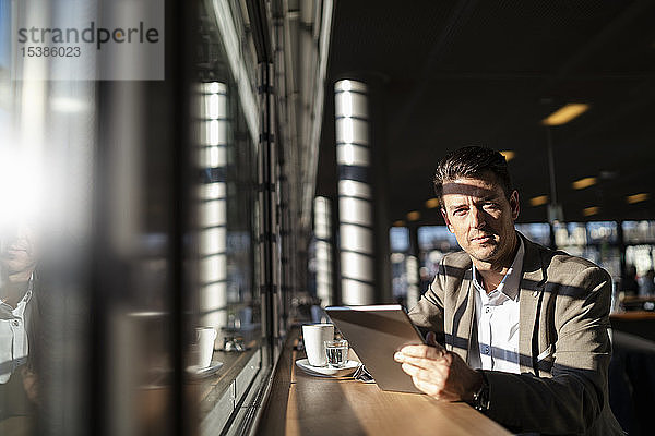Porträt eines Geschäftsmannes mit Tablette am Fenster in einem Café