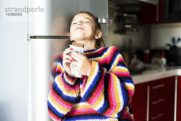 Mädchen in gestreiftem Pullover in der heimischen Küche beim Schokoladenessen