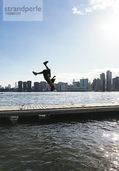 USA  New York  Brooklyn  junger Mann beim Rückwärtssalto auf dem Pier vor der Skyline von Manhattan