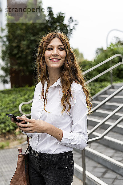 Junge Geschäftsfrau geht die Treppe hinunter und benutzt ein Smartphone