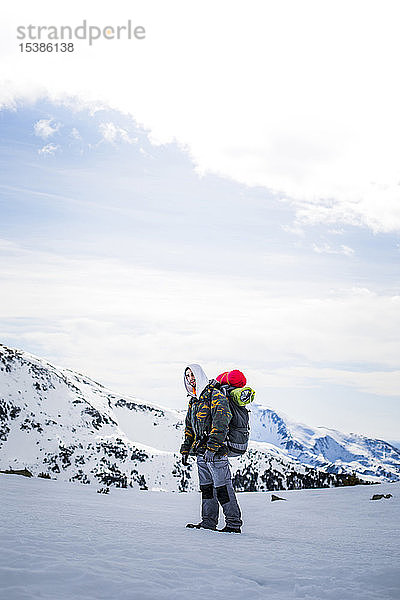 Junger Mann mit Rucksack  im Hintergrund schneebedeckte Berge