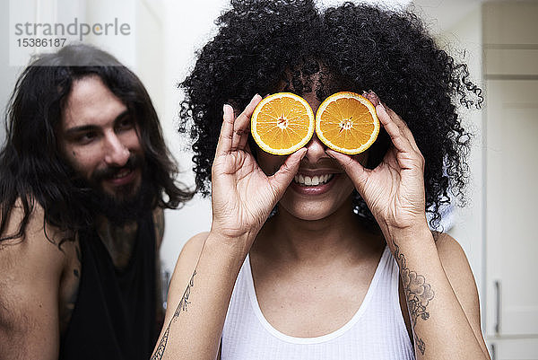 Glückliche junge Frau bedeckt ihre Augen in der Küche mit Orangen
