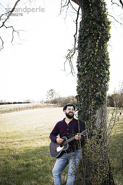 Mann spielt Gitarre an einem Baum auf einer Wiese