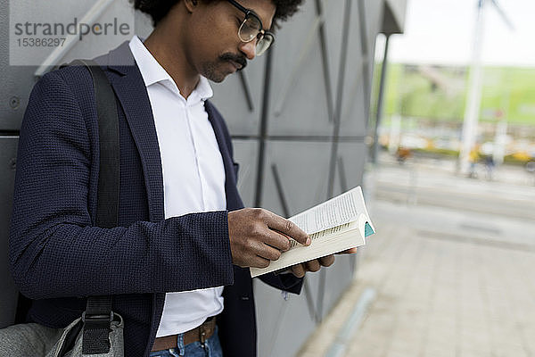 Geschäftsmann steht an einer Mauer in der Stadt und liest Buch