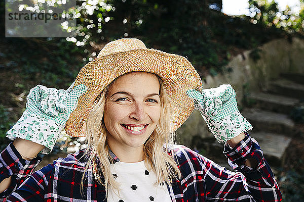 Junge blonde Frau mit Strohhut und grünen Gartenhandschuhen