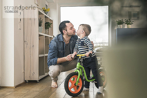 Vater küsst Sohn mit einem Balance-Fahrrad zu Hause