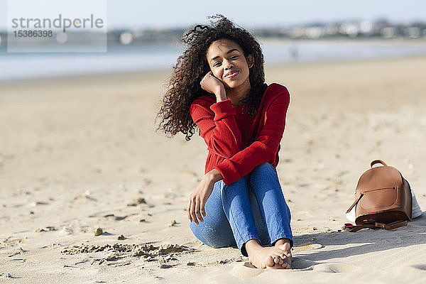Porträt einer lächelnden jungen Frau am Strand sitzend
