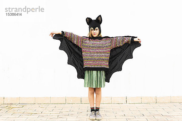 Bildnis eines Mädchens in Fledermauskostüm  das vor einer weißen Wand Flügel ausbreitet