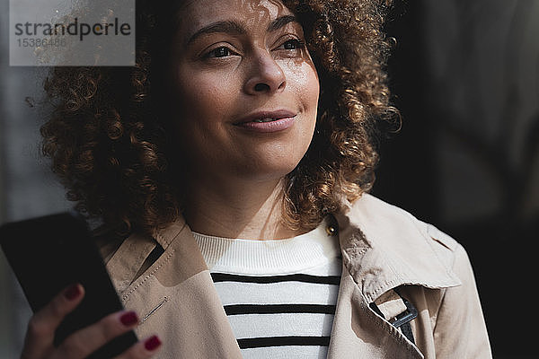 Porträt einer lächelnden Frau mit Handy in der Hand