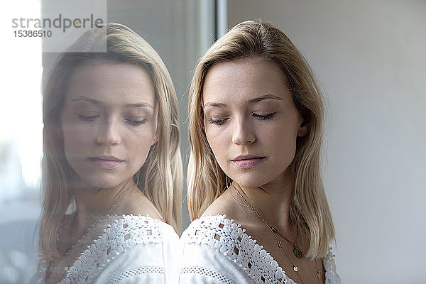 Porträt einer blonden jungen Frau und ihre Reflexion auf einer Fensterscheibe