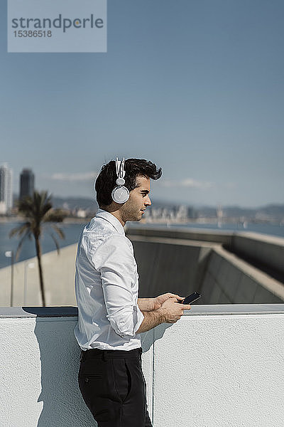 Profil eines Geschäftsmannes  der mit Kopfhörer und Smartphone auf der Dachterrasse Musik hört