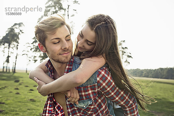 Lächelnder junger Mann trägt seine Freundin huckepack auf der Wiese
