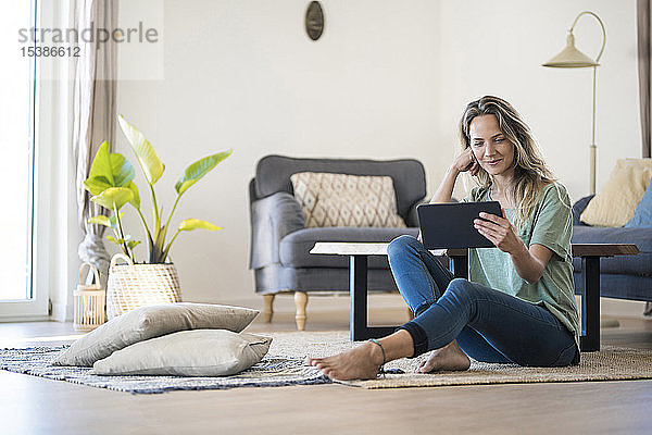 Lächelnde Frau sitzt zu Hause mit Tablette auf dem Boden
