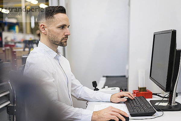 Geschäftsmann mit Computer am Schreibtisch in einer Fabrik