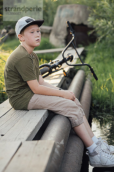 Seriöser Junge mit BMX-Fahrrad auf der Strandpromenade sitzend