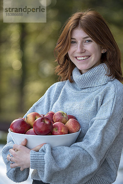 Porträt eines rothaarigen Teenagers  der eine Schale mit Äpfeln hält