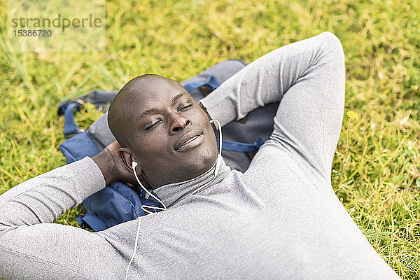 Porträt eines Geschäftsmannes  der auf einer Wiese liegt und mit Kopfhörern Musik hört