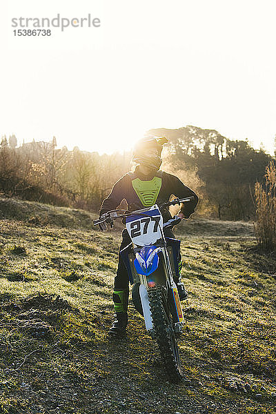 Motocross-Fahrer steht bei Sonnenuntergang auf der Rennstrecke