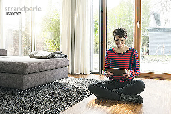 Porträt einer Frau  die mit einem digitalen Tablett auf dem Boden eines Wohnzimmers sitzt