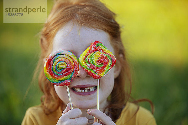 Glückliches Mädchen bedeckt die Augen mit Lollipops