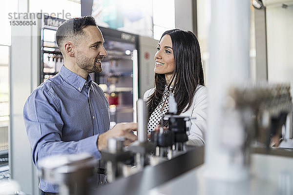 Lächelnder Geschäftsmann und Geschäftsfrau im Gespräch an einer Maschine in einer modernen Fabrik
