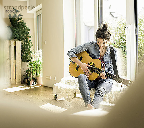 Frau sitzt zu Hause am Fenster und spielt Gitarre