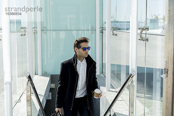 Porträt eines Geschäftsmannes mit Sonnenbrille  Kaffee zum Mitnehmen und Gepäck auf der Treppe